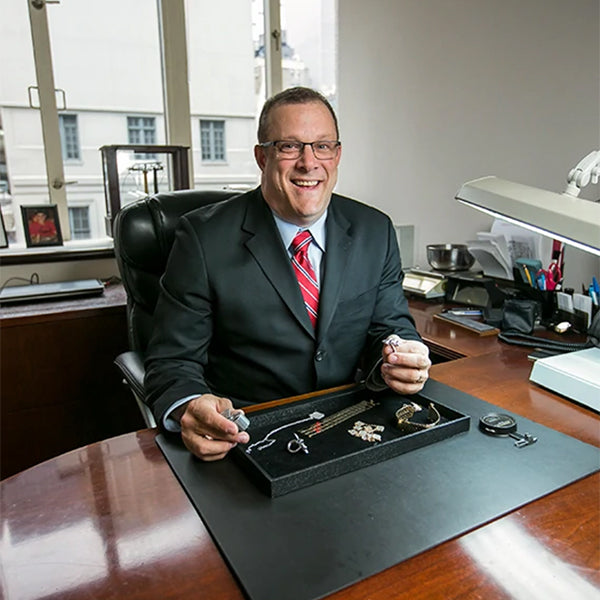 Photo of Andrew Fabrikant evaluating jewelry at desk.